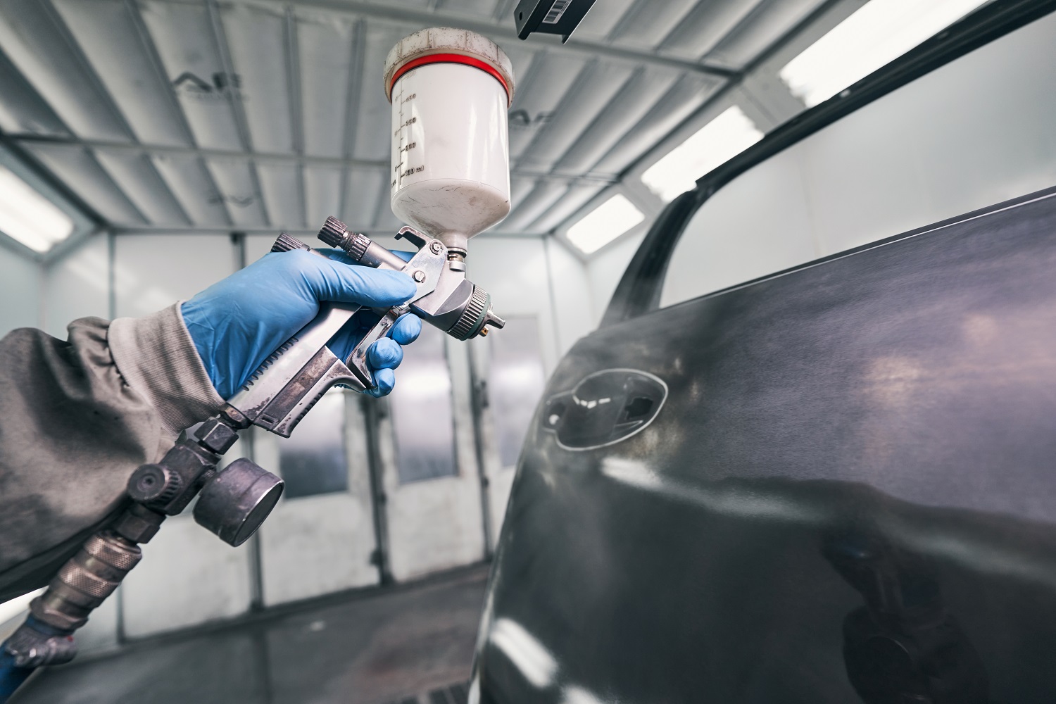 Auto workshop worker painting car door with spraying pistol