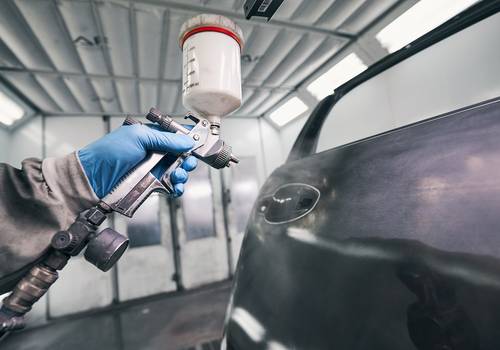 Auto workshop worker painting car door with spraying pistol